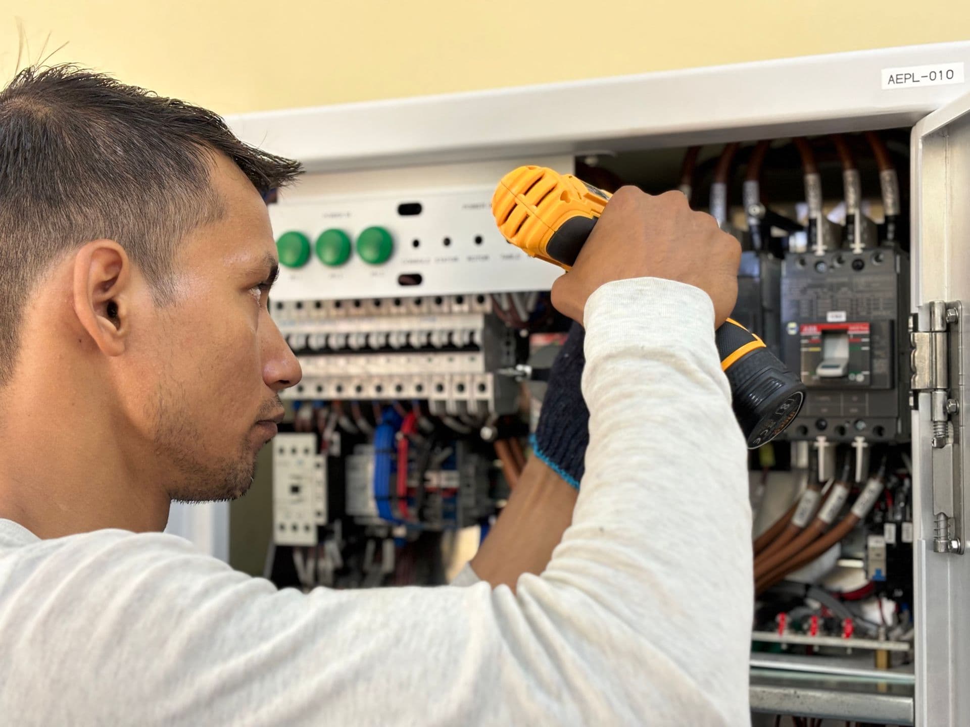 Electrician driving a screw inside an open breaker panel filled with wiring