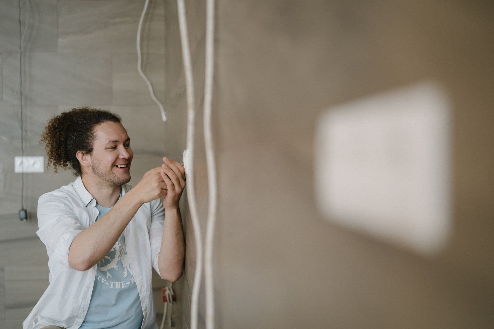 Electrician working on a wall outlet in a room stripped back for renovation
