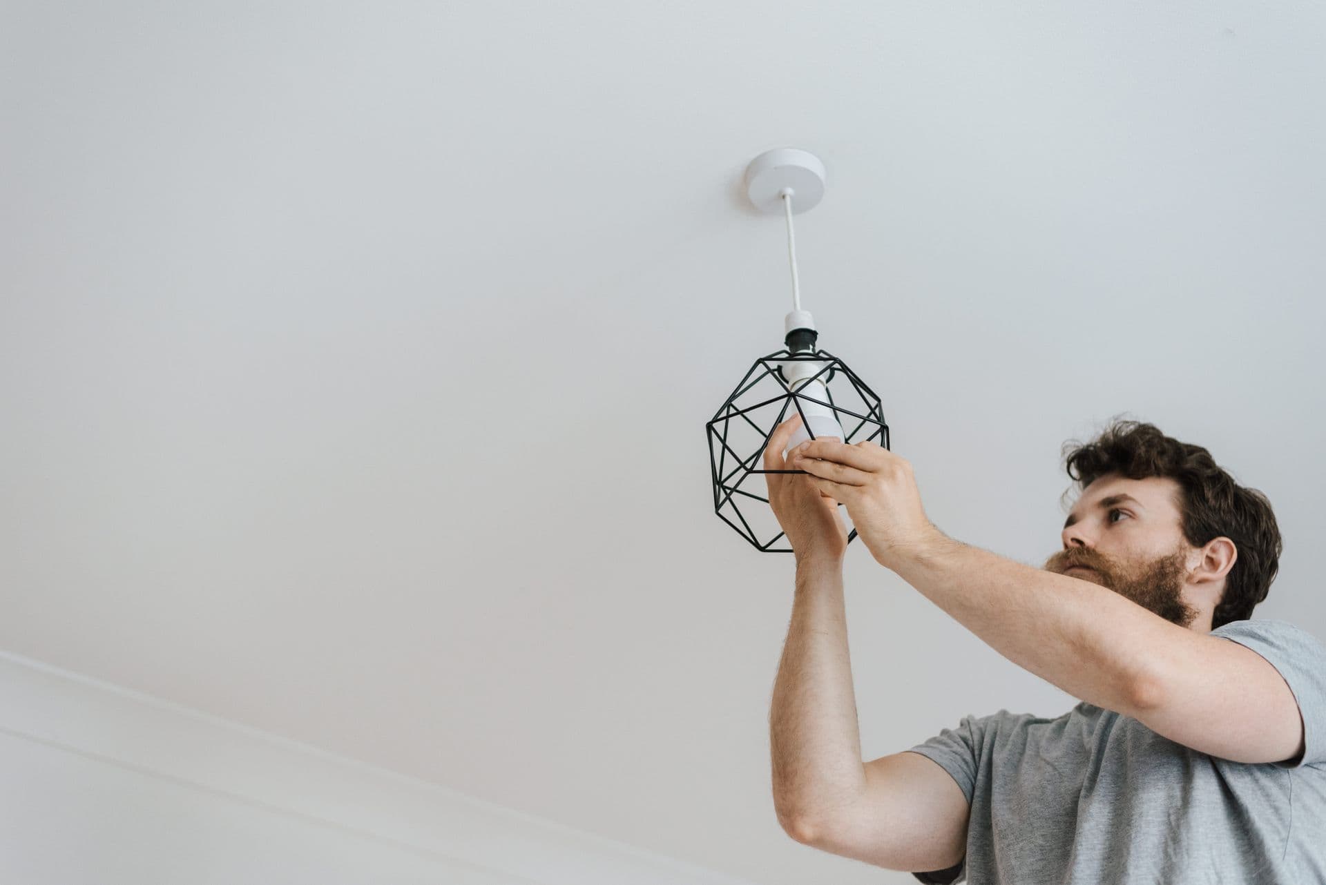 Worker fitting a bulb into a newly hung geometric ceiling pendant