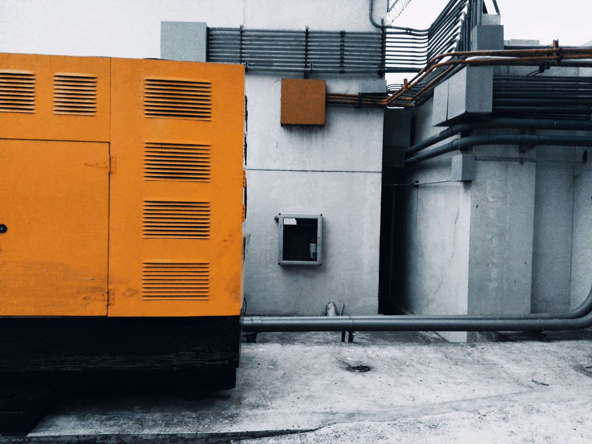 Outdoor generator enclosure with conduit and piping running along a concrete wall