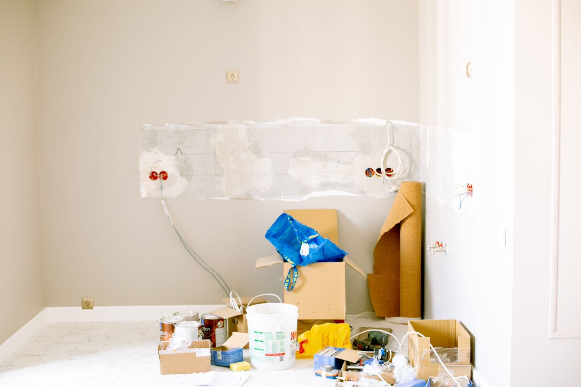 Room mid-renovation with loose wiring at the wall and paint cans on the floor