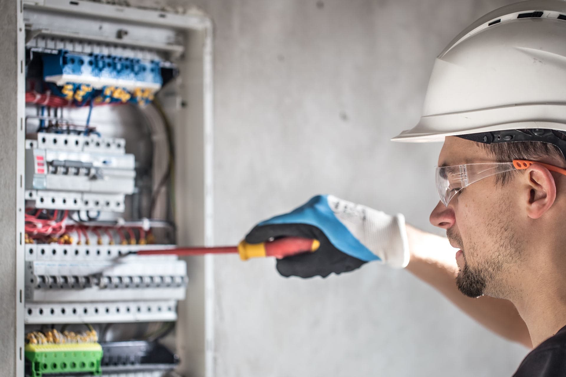 A technician using an insulated screwdriver on the breakers of a wall-mounted distribution board