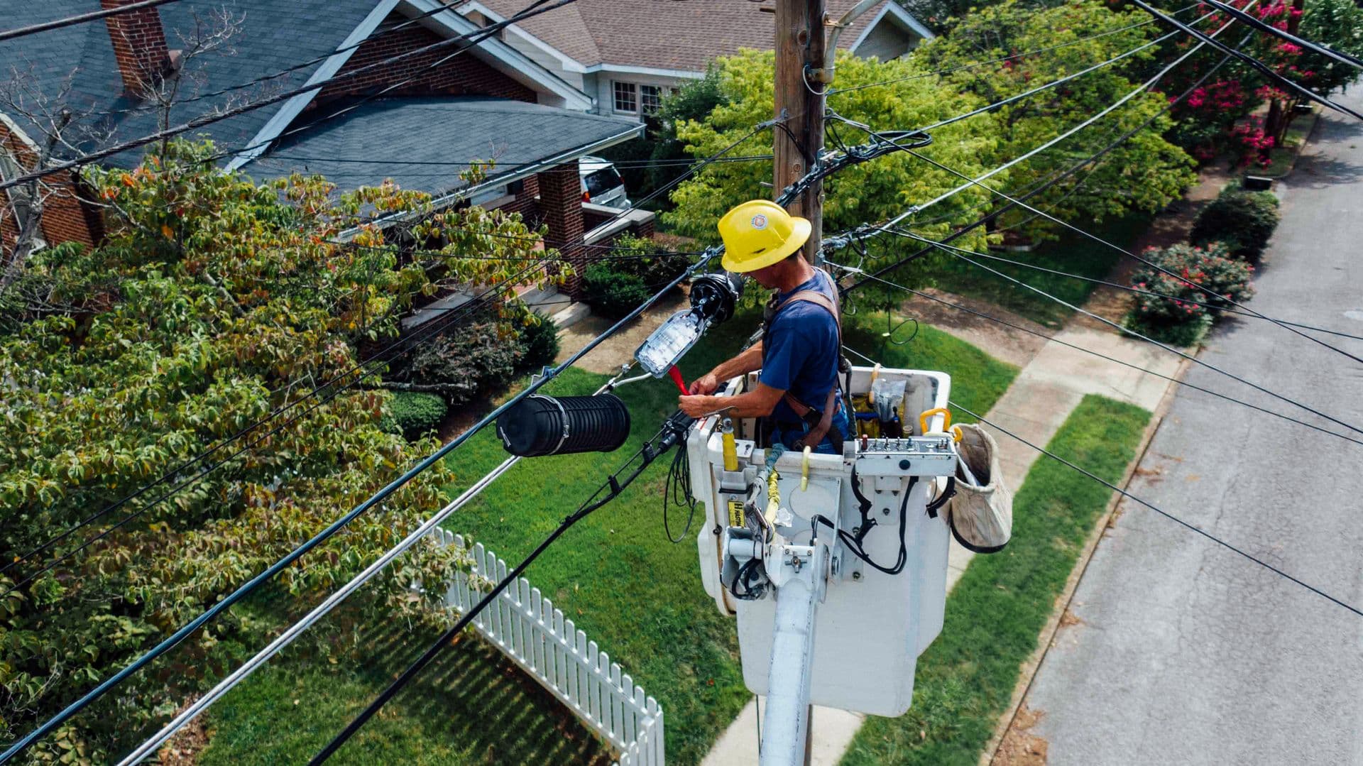 Line worker in a bucket lift repairing overhead wires above a residential street