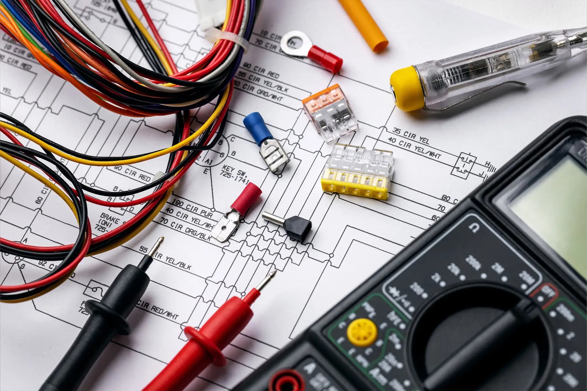 A multimeter and hand tools with wire connectors laid out on a printed wiring schematic